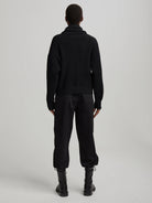 Black mock neck sweater with prominent vertical ribbing. Model viewed from the back.