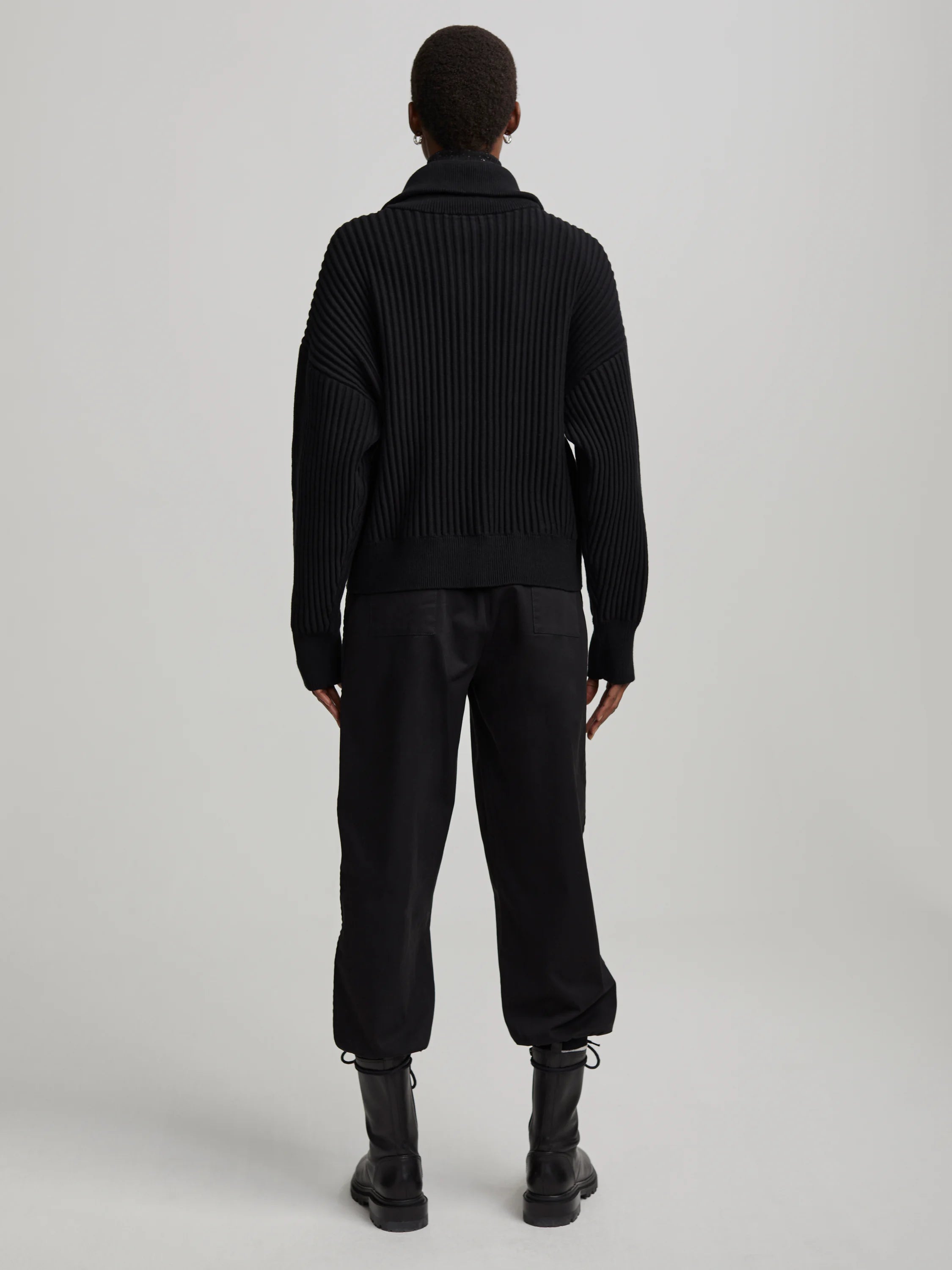 Black mock neck sweater with prominent vertical ribbing. Model viewed from the back.