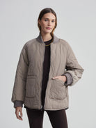 Taupe quilted bomber jacket with wavy pattern, gray ribbed collar & cuffs, front pockets, and silver zipper.