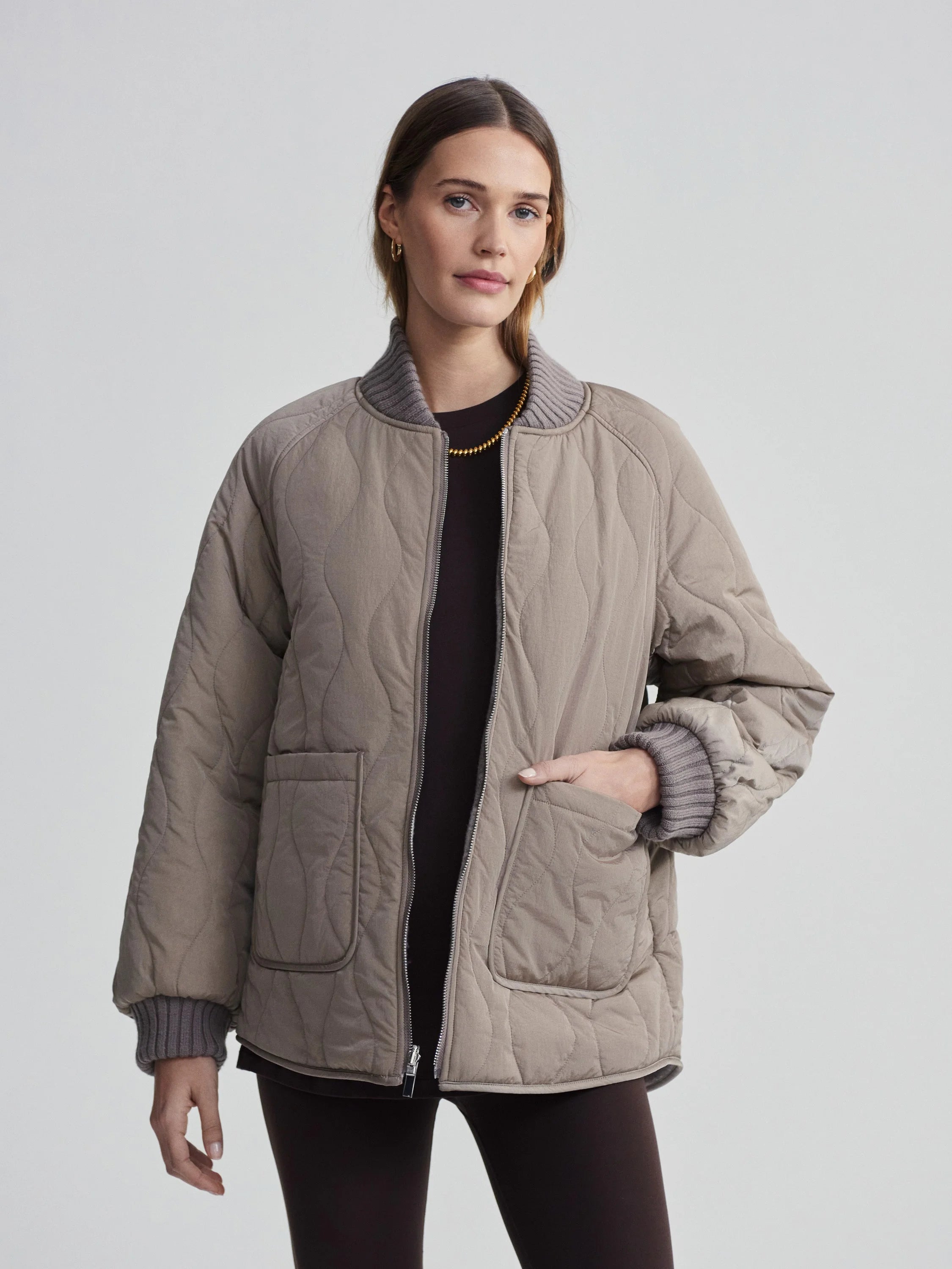 Taupe quilted bomber jacket with wavy pattern, gray ribbed collar & cuffs, front pockets, and silver zipper.