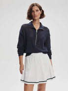 Navy blue, half-zip, open knit sweater; gold zipper.  Model also wears white pleated skirt with dark green trim.