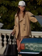 Tan, double-breasted short trench coat with wide collar, dark buttons, and belt.