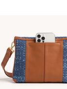Brown leather bag with woven blue denim in a checkerboard pattern. Front leather pocket holds a phone. Gold hardware.