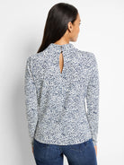 Cream-colored top with dark blue speckled pattern, high neck, keyhole back. Long sleeves.
