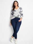 Light gray V-neck sweater with dark gray abstract pattern.  Model also wears dark wash jeans and white sneakers.