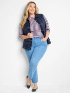 Navy blue quilted puffer vest with gold buttons.  Model wears it over a pink and white striped shirt.