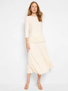 Off-white sweater with a feather fringe hem, paired with a pleated off-white midi skirt.