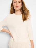 Off-white sweater, three-quarter sleeves, textured knit body, and a bottom border of  long, light beige feather fringe.