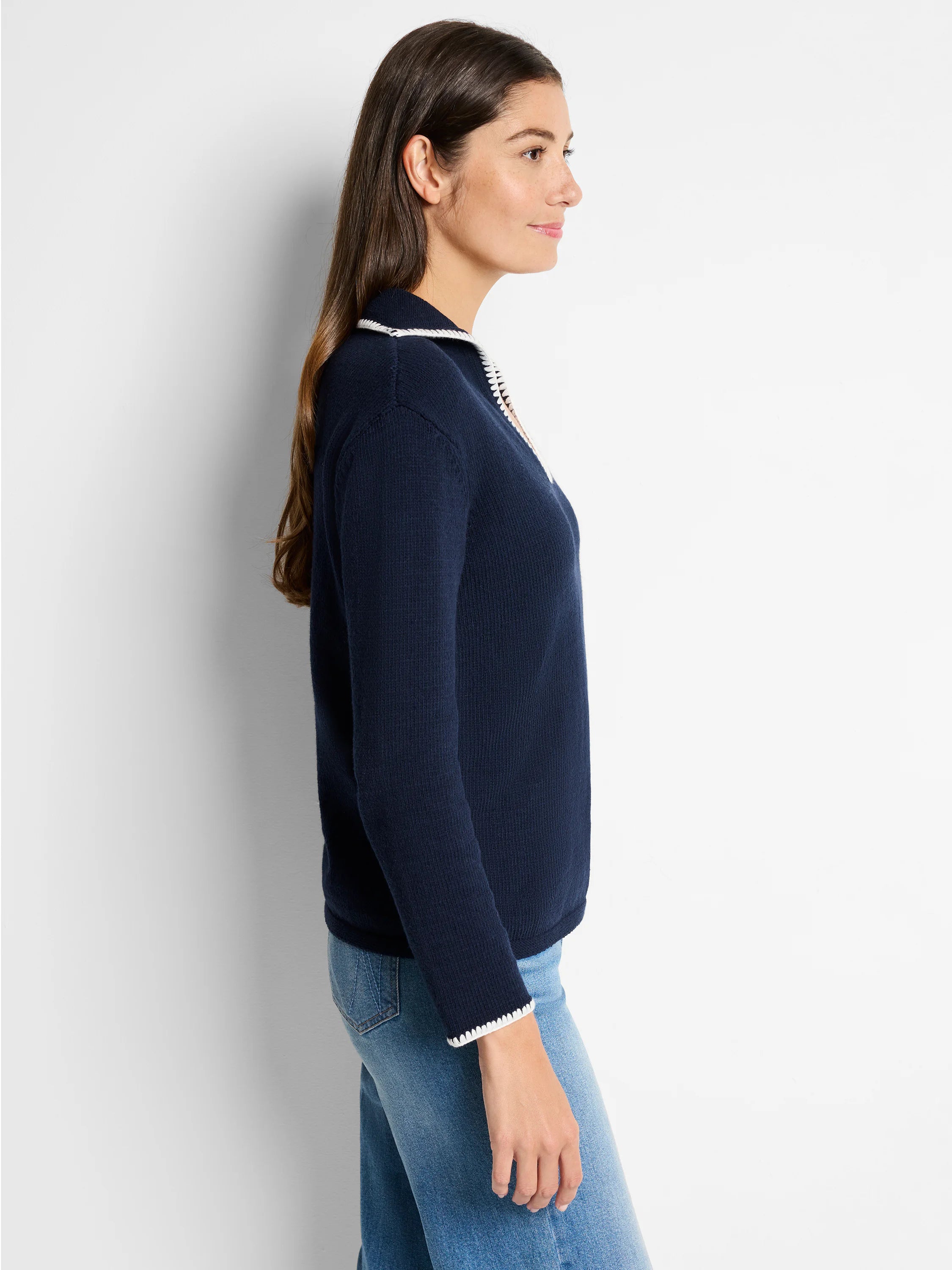 Navy blue sweater with off-white blanket stitch trim at collar and cuffs. Long sleeves. Side profile view.