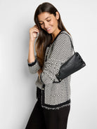 Black and off-white patterned sweater jacket with frayed edges.  Model also carries a black leather handbag.