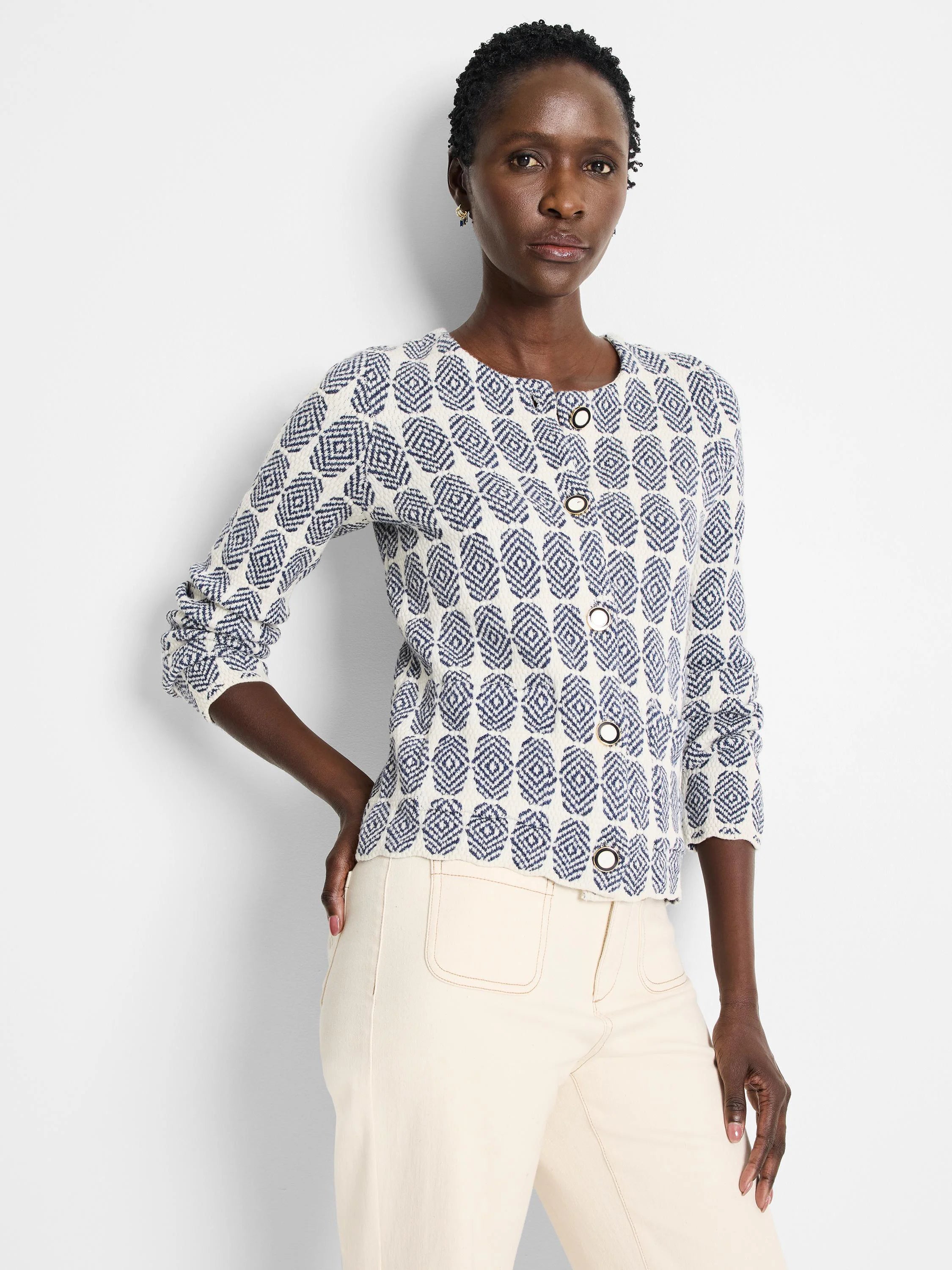 Off-white knit jacket with a navy blue geometric pattern and gold buttons.  Long sleeves, close-fitting.