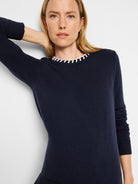 Navy blue sweater with off-white trim at neckline. Long sleeves, knit fabric.