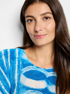 Image of woman wearing a blue and white tie-dye sweater.  The sweater has a loose fit and a round neckline.