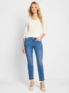Off-white V-neck sweater, long sleeves.  Model wears medium-wash blue jeans with frayed hems.