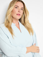 Light blue, long-sleeve blouse with a V-neck and elasticized cuffs.  Model is wearing the garment.