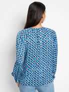 Long-sleeve blue top with a repeating abstract pattern in shades of blue, beige, and black.  Back view.