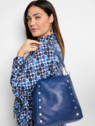 Deep blue leather shoulder bag with silver studs.  Features a textured surface.  Model wears a blue and white patterned...