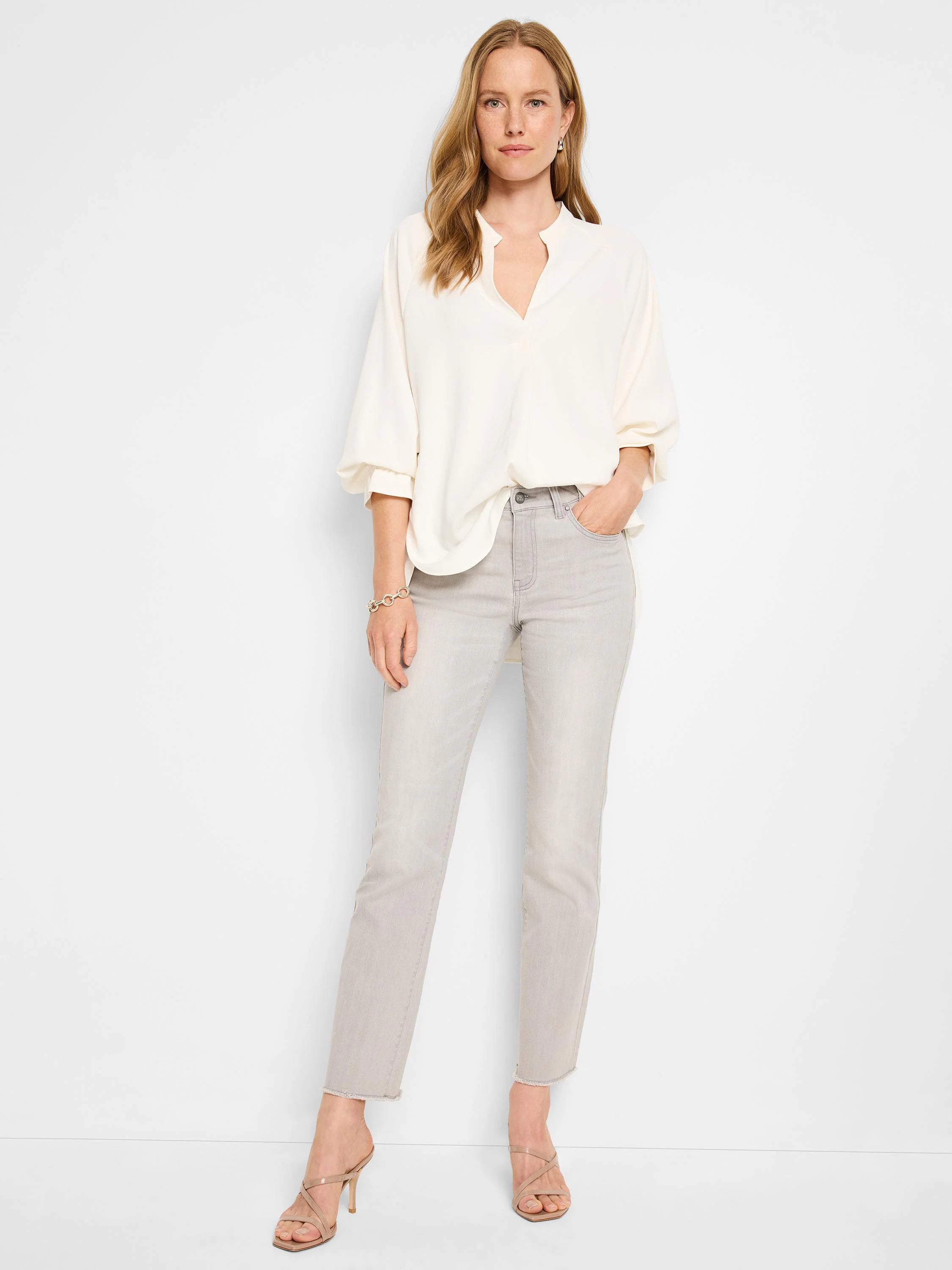 Light gray mid-rise demi boot jeans, shown on a standing model, feature a frayed hem.