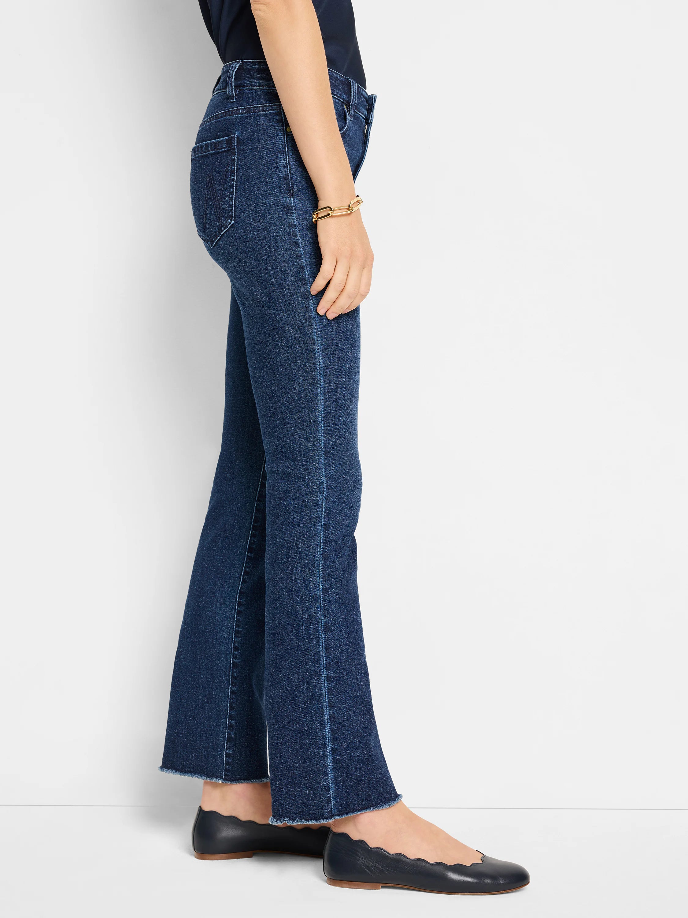 Dark blue mid-rise demi boot jeans with a subtle leg seam and frayed hem, worn by a model in profile.