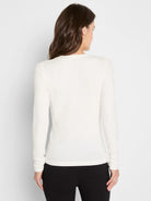 Back view of a woman wearing a cream, long-sleeve, fitted ribbed knit top.