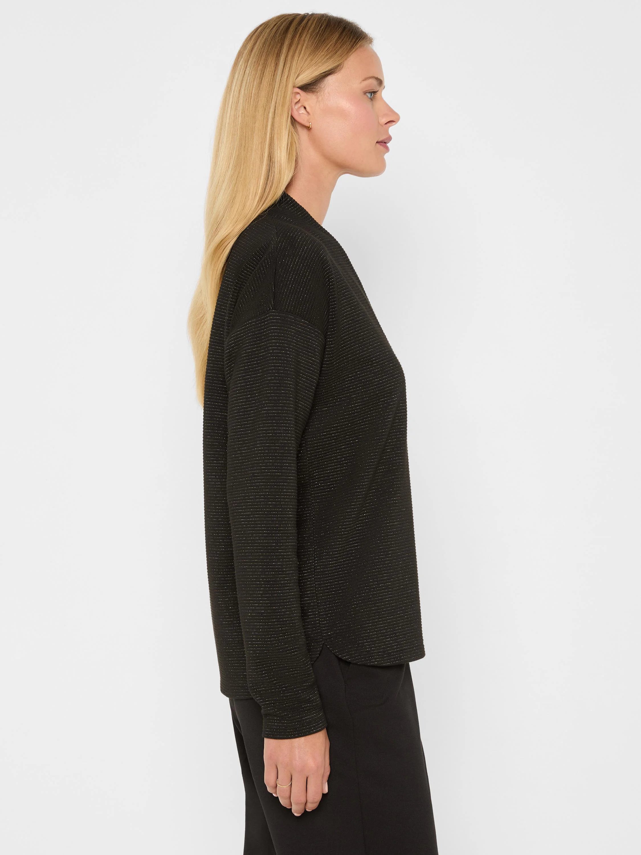 Model in profile wearing a black long-sleeve top with thin gold metallic stripes. Relaxed fit.