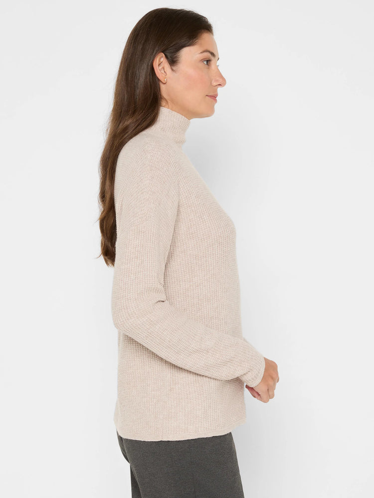 Light beige waffle knit turtleneck sweater with long sleeves, worn by a model.