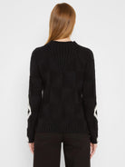 Black sweater with a raised diamond knit pattern, ribbed mock neck, and white zig-zag details on the sleeves.