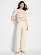 A relaxed cream and pink striped mesh sweater is paired with fitted high-rise, wide-leg beige pants.