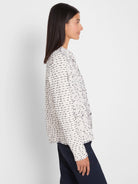 Cream nep weave knit jacket with dark flecks. Features fringed edges, a collarless design, and metal grommet details.