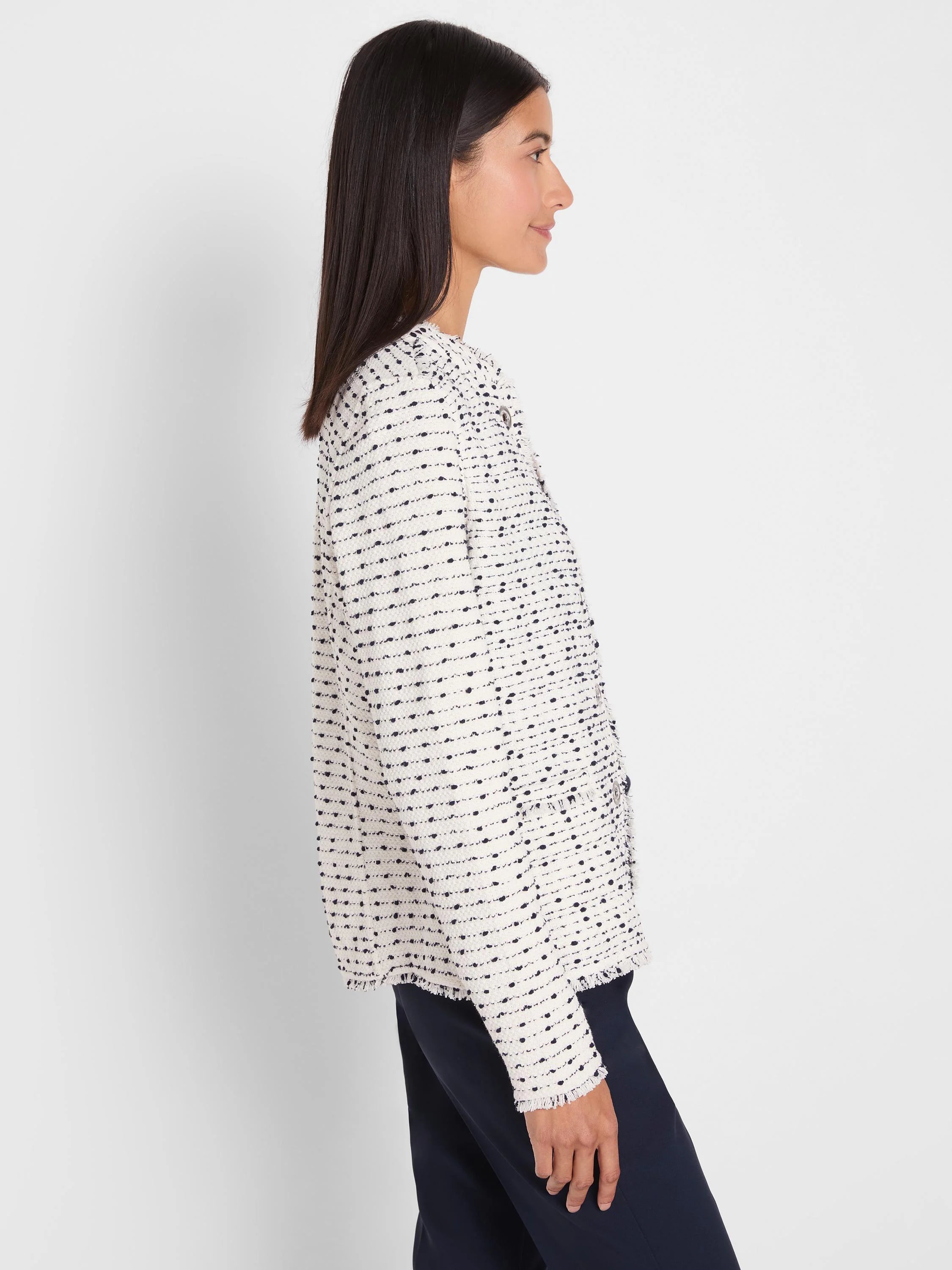 Cream nep weave knit jacket with dark flecks. Features fringed edges, a collarless design, and metal grommet details.