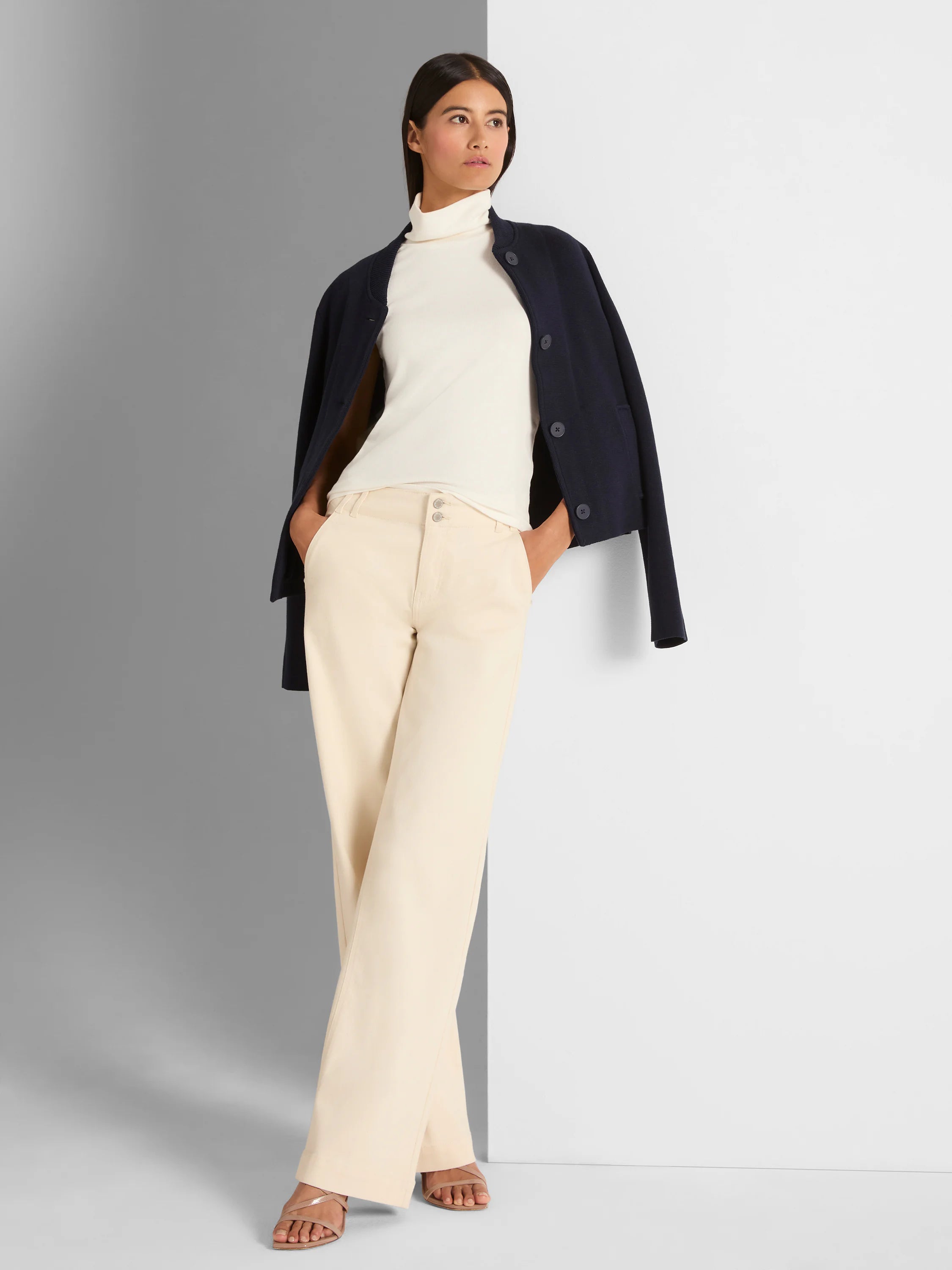 Dark navy knit bomber jacket with ribbed round neck and button front, worn open over a cream turtleneck.