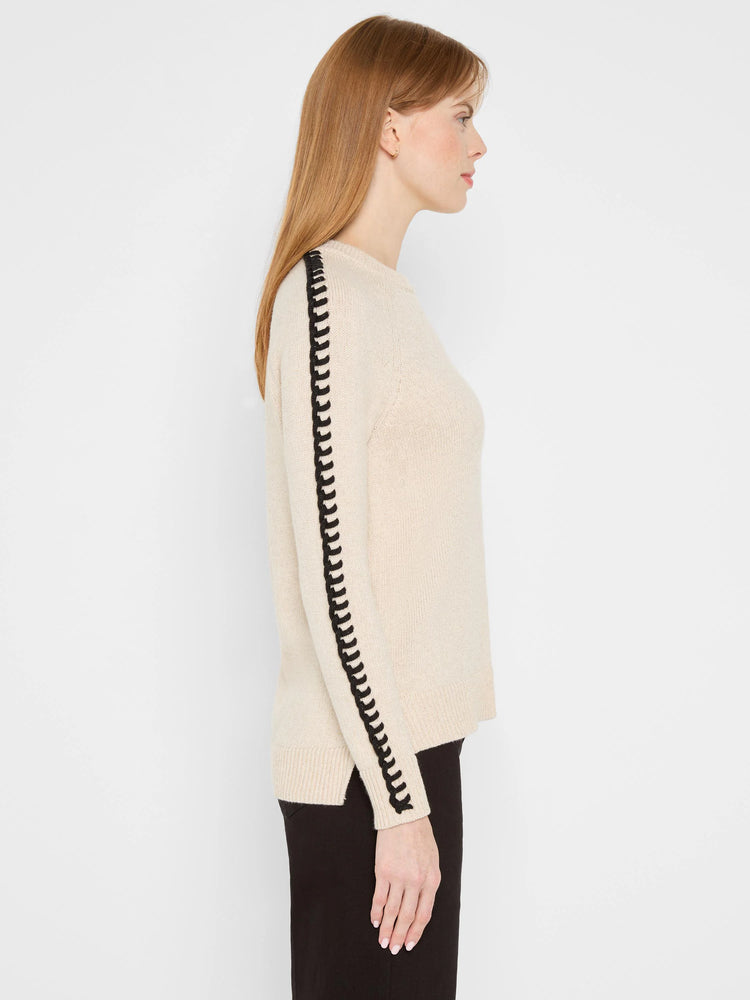 Light beige metallic sweater with black looped trim down the outer sleeves, worn by a model.