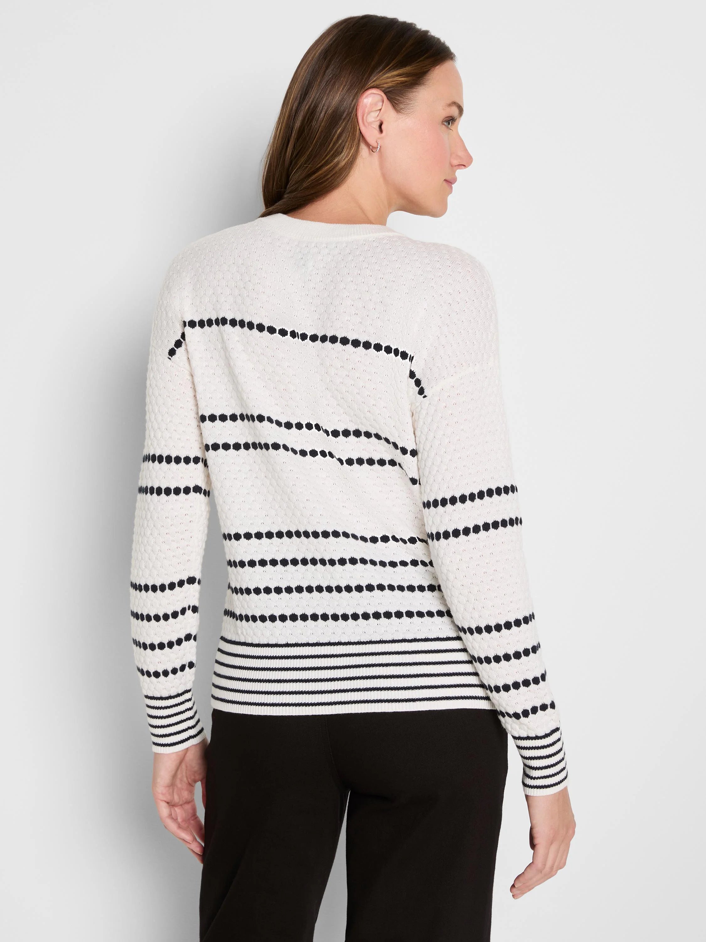 Off-white sweater with black rows of dots on body & sleeves, plus striped cuffs & hem. Model from back.