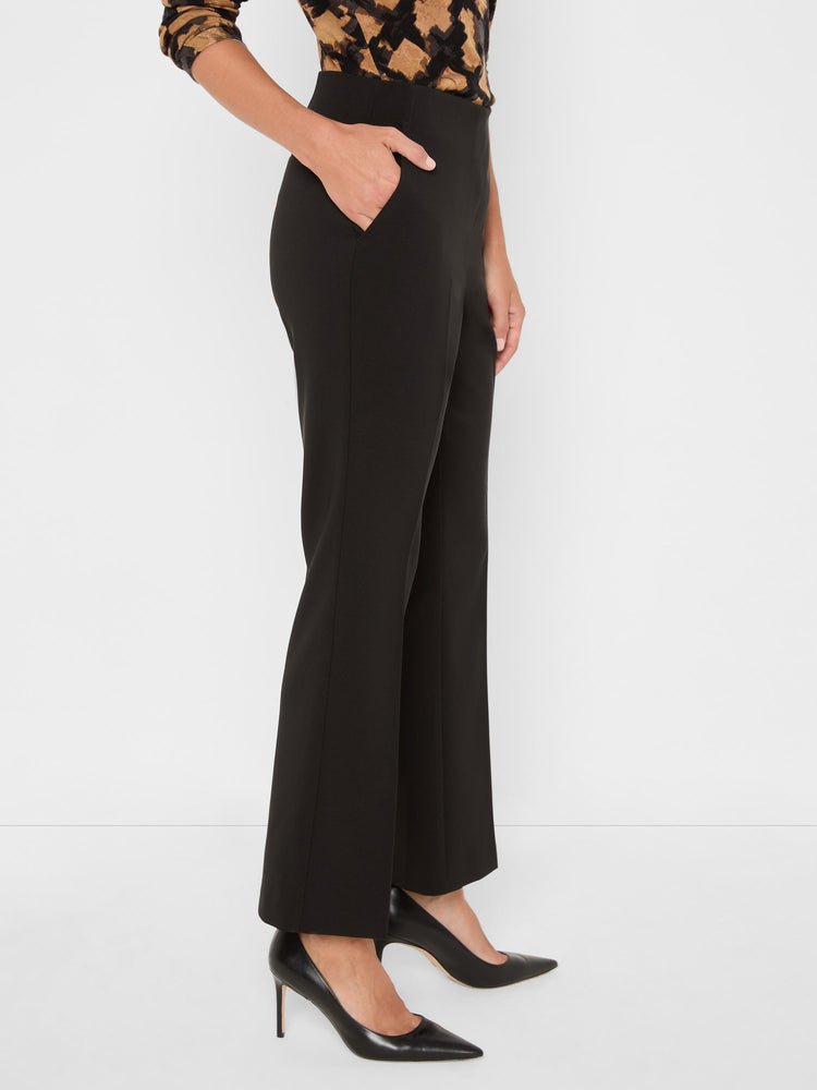 Black high-waisted trousers with a subtle flare and slash pockets are worn ankle length.