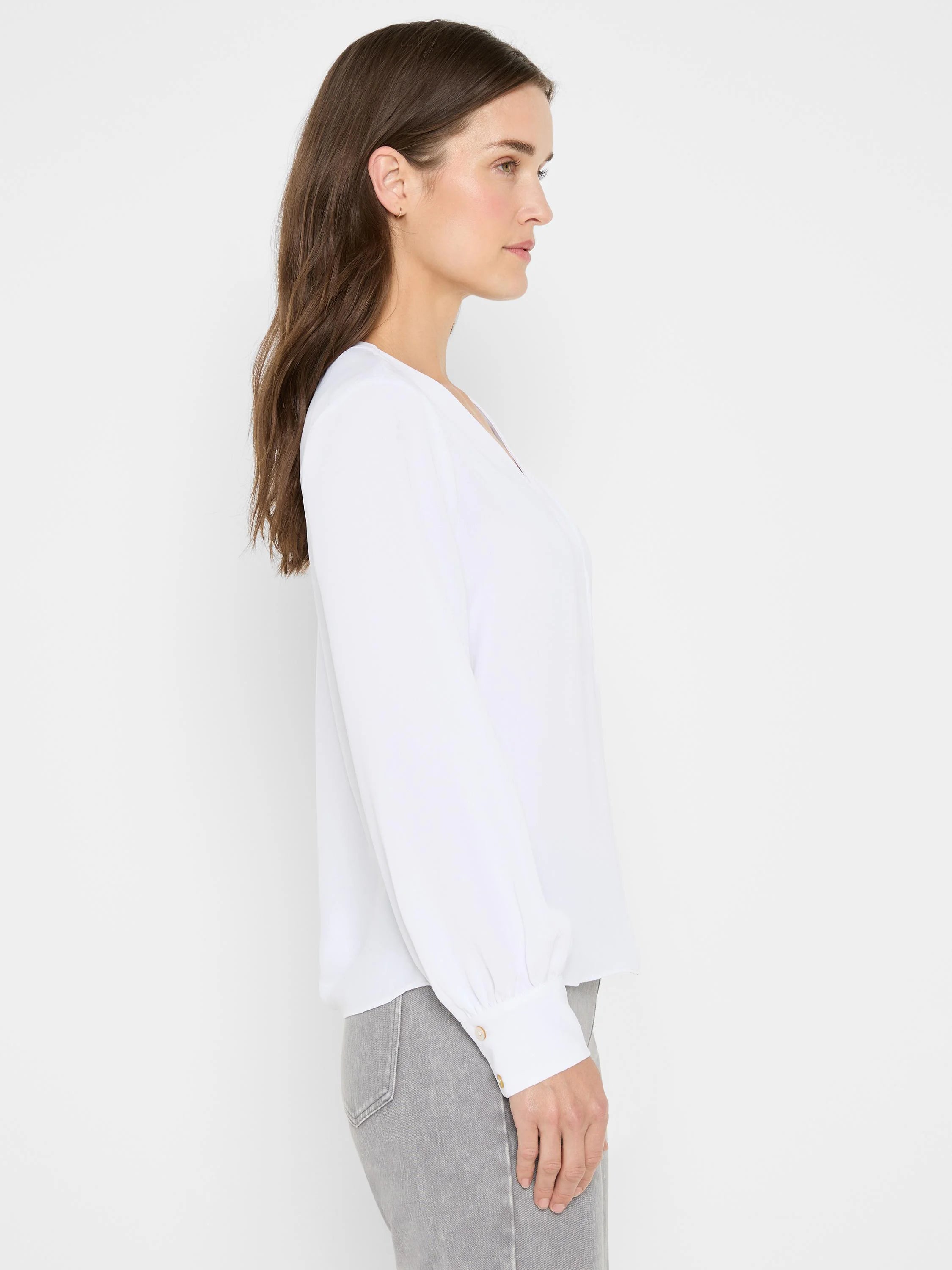 White V-neck top with long sleeves and light brown buttoned cuffs, shown on a model from the side.