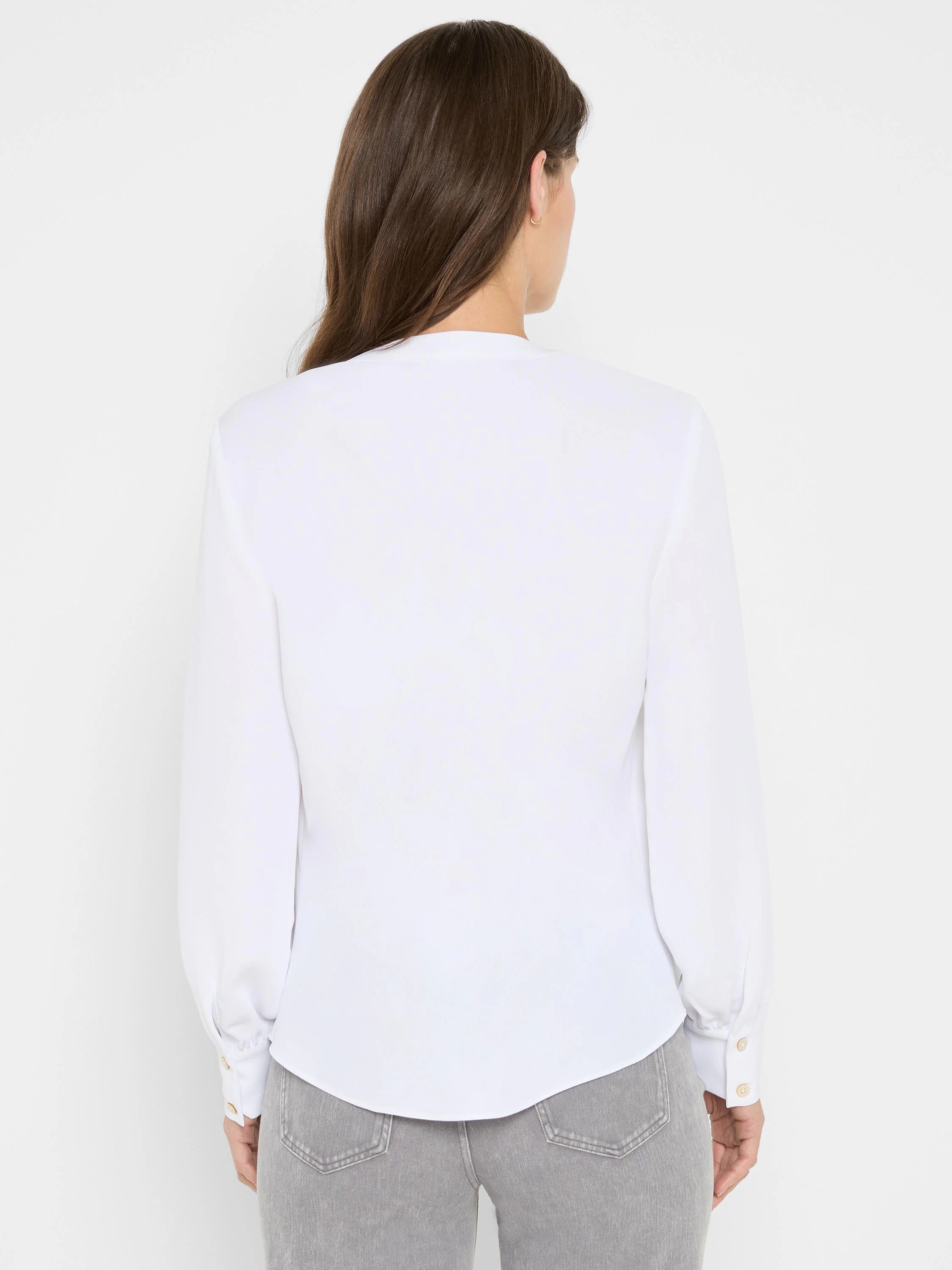 Back view of a white long-sleeved top with light buttoned cuffs and a curved hemline.