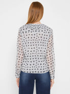 Light grey blouse with dark grey dotty square pattern, featuring a ruffled neckline. Worn from the back.