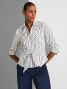 A white and blue striped button-down shirt features front flap pockets and a casual tied knot at the waist hem.