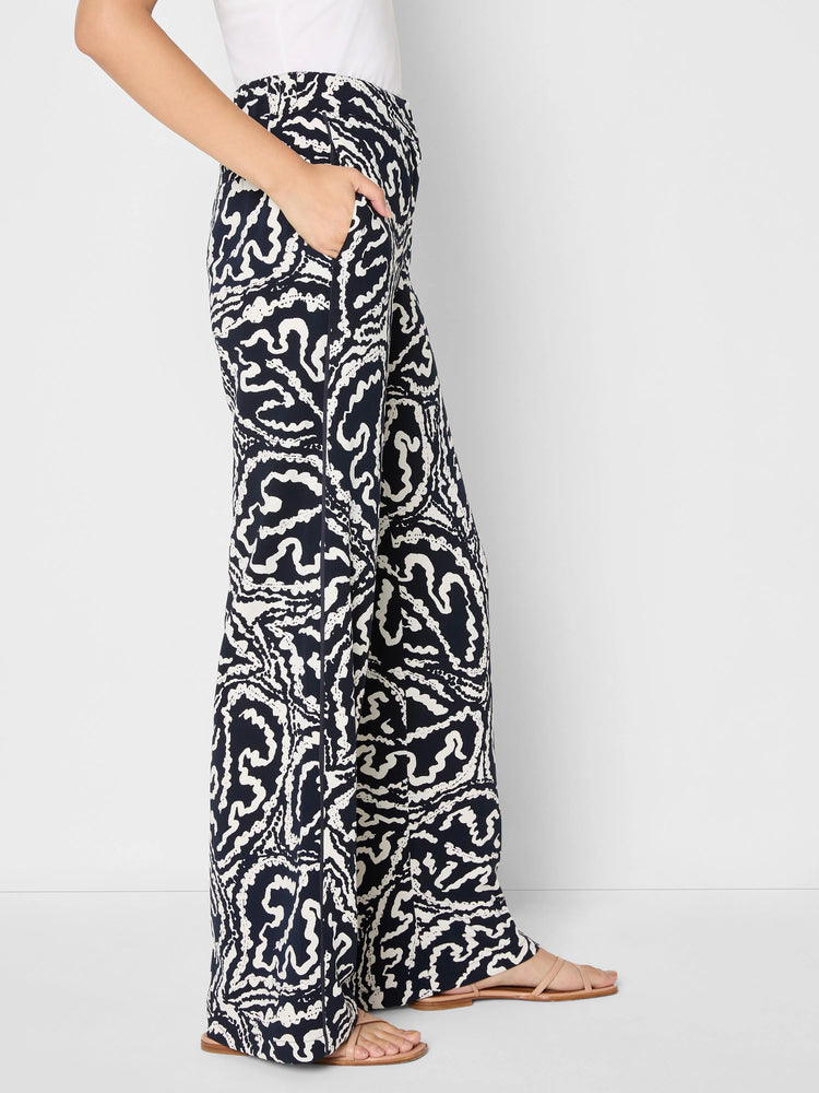 Indigo wide-leg pants with an off-white abstract leaf pattern. A hand is in the side pocket.