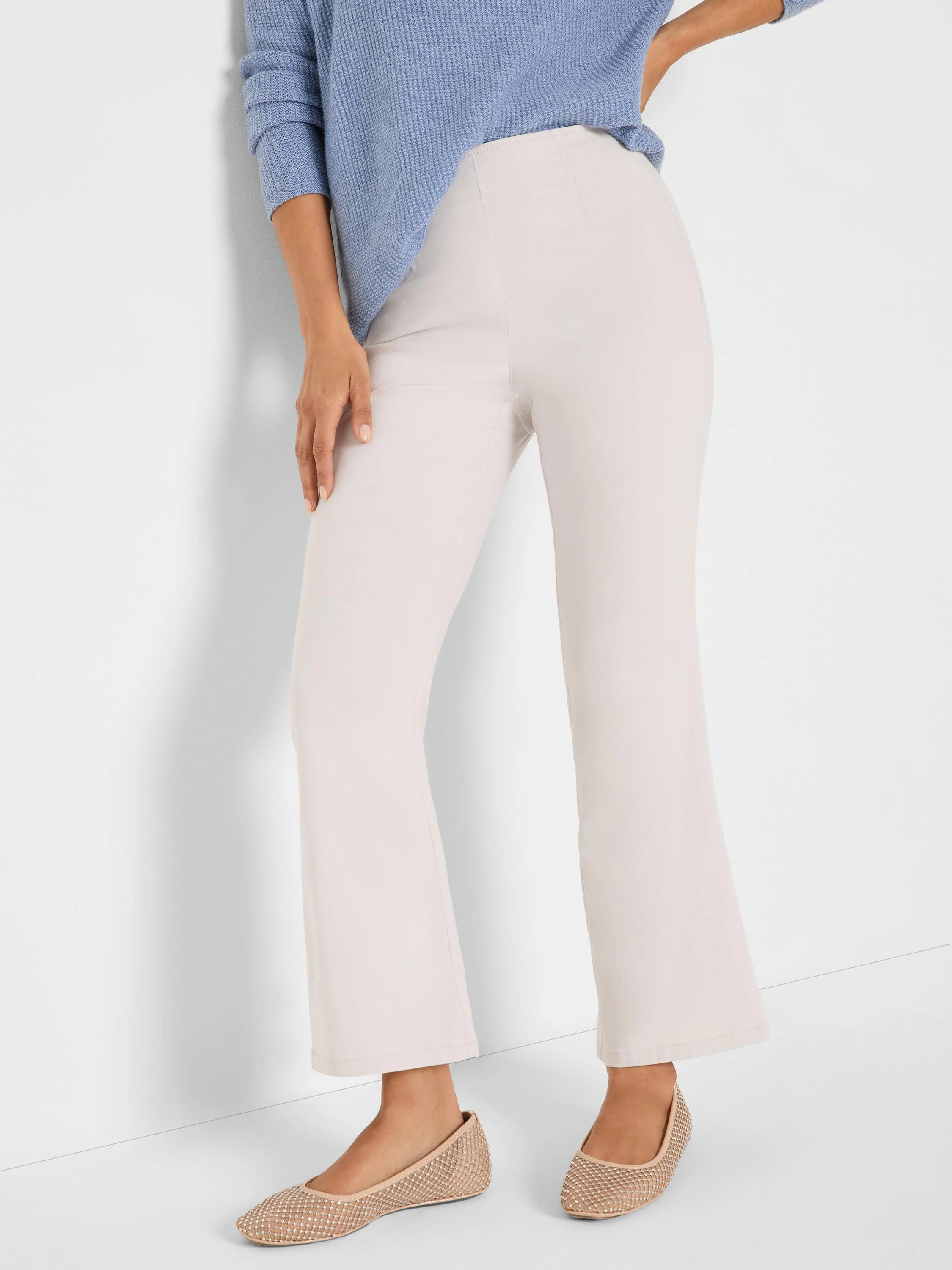 Light beige high-waisted bootcut pants with smooth fabric, worn by a model.