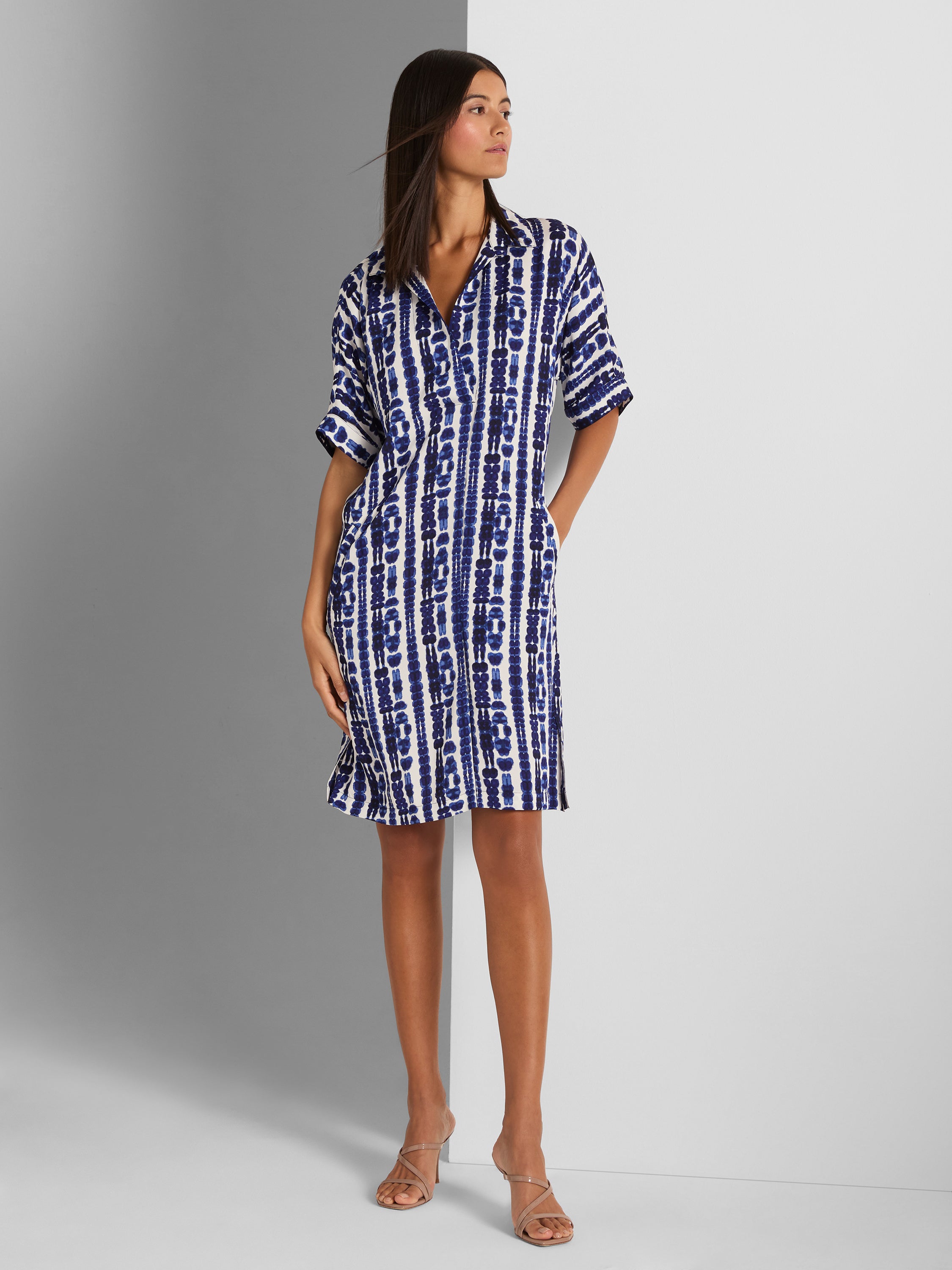 A relaxed blue and white tie-dye stripe shirtdress with short sleeves and pockets is worn above the knee.