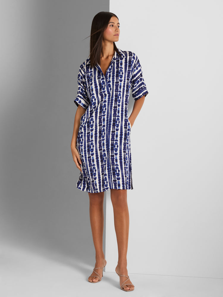 A relaxed blue and white tie-dye stripe shirtdress with short sleeves and pockets is worn above the knee.