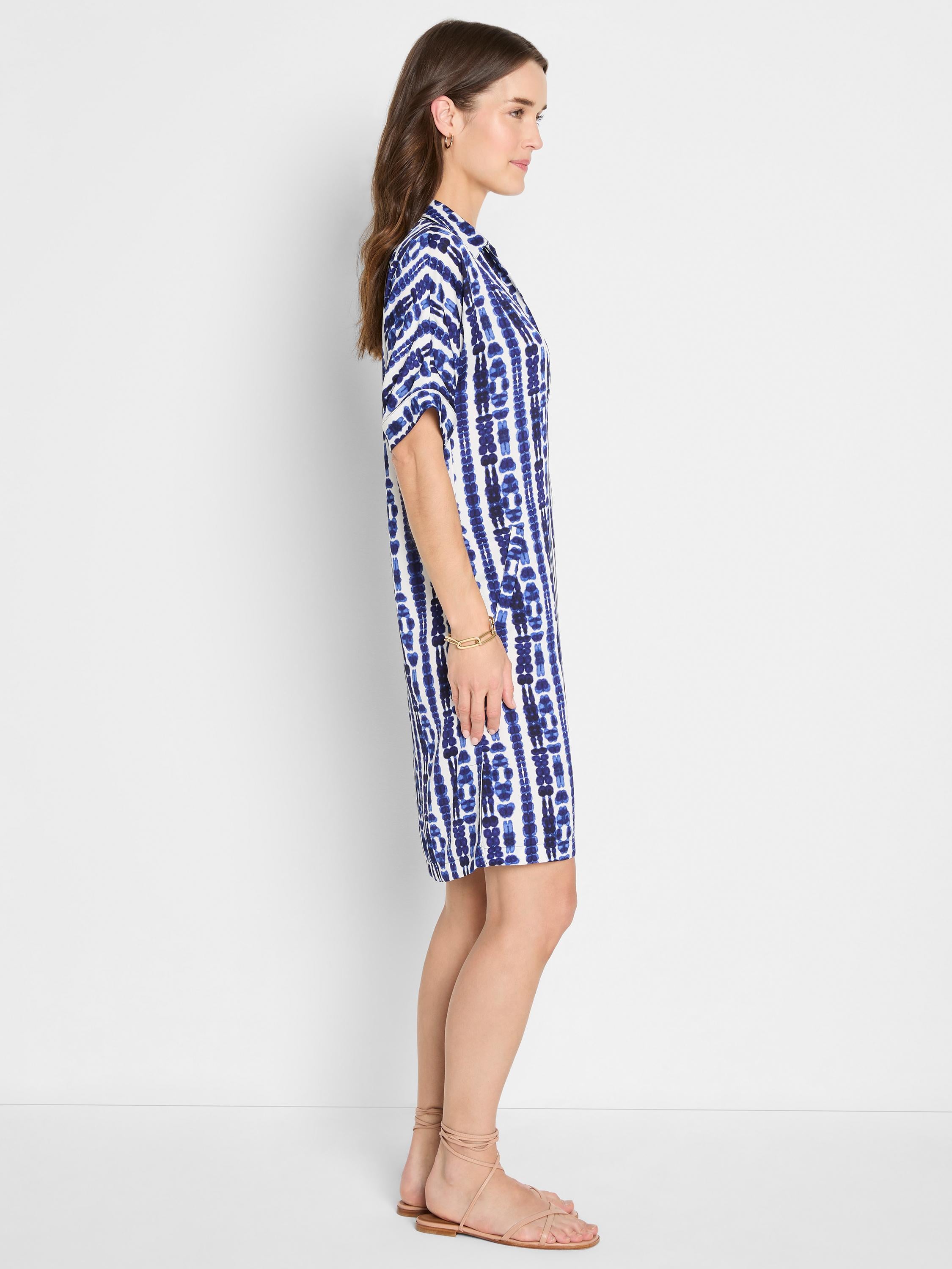 She wears a relaxed blue and white tie-dye shift dress featuring a collar and short cuffed sleeves.
