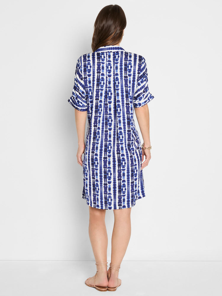 A relaxed, short blue and white shibori shirtdress with rolled short sleeves is worn by the model.