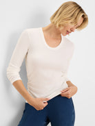Cream long-sleeve, U-neck tee with prominent rib knit texture and ruched details on the left side and sleeves.