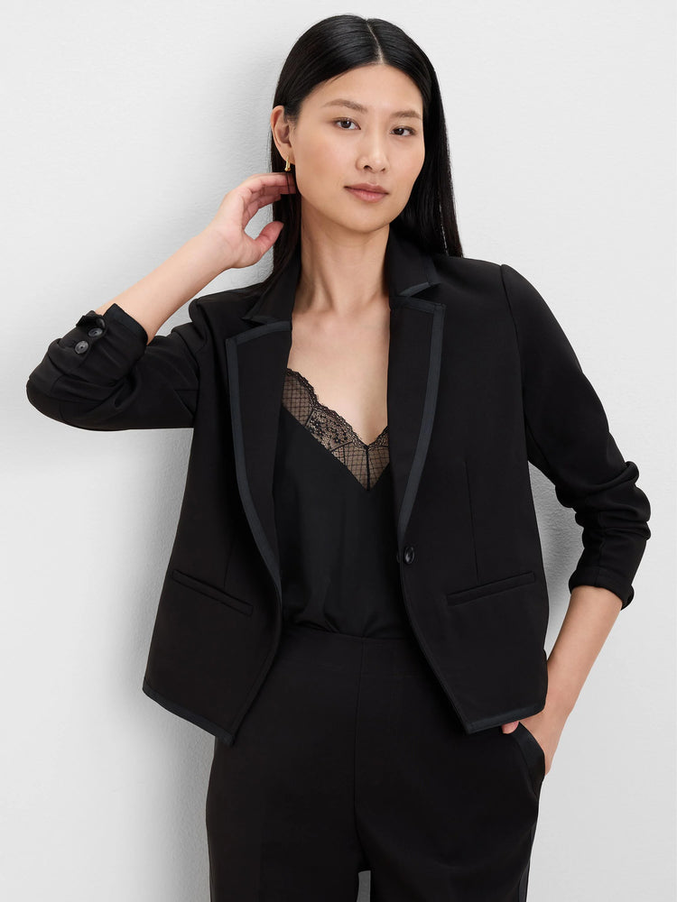Black blazer with black grosgrain trim on lapels and cuffs. Features a single button closure and front flap pockets.