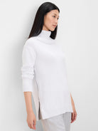 White foldover turtleneck sweater with long sleeves, ribbed cuffs/hem, and a partially unzipped side vent.