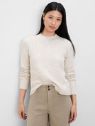 Cream roll neck sweater with a prominent herringbone weave pattern throughout. Features ribbed collar, cuffs, and hem.