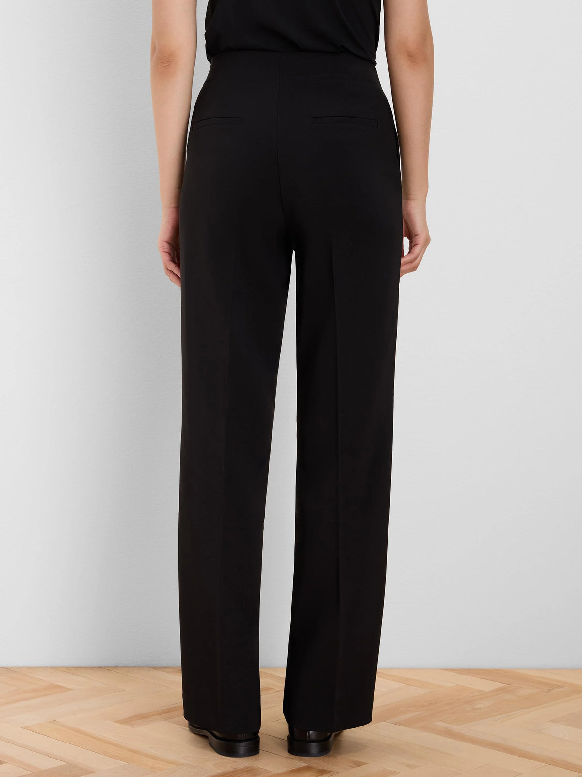 Black wide leg high-waisted pants, shown from the back, with two flat welt pockets.