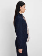 Dark blue denim jacket with a high collar and elastic cuffs, worn by a model in profile view.